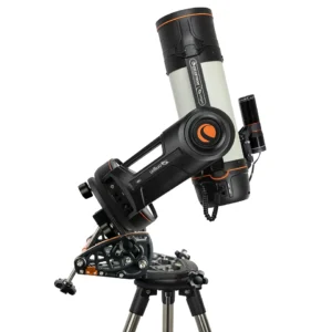 Dieses Bild zeigt das Celestron Origin Intelligent Home Observatory, ein hochmodernes, vollautomatisches "Smart-Teleskop". Hier ist eine detaillierte Beschreibung für den Alt-Text: Gerät: Zu sehen ist das Celestron Origin, ein kompaktes astronomisches System, das Optik, Kamera und Computersteuerung in einem Gehäuse vereint. Es basiert auf einem 6-Zoll Rowe-Ackermann Schmidt Astrograph (RASA) Design. Aufbau: Das weiße Teleskoprohr ist auf einer einarmigen, schwarzen Gabelmontierung befestigt. Das gesamte System sitzt hier auf einer speziellen Polhöhe (Wedge), die wiederum auf einem Edelstahlstativ montiert ist. Diese "Wedge" ermöglicht eine parallaktische Ausrichtung, was für die Astrofotografie längere Belichtungszeiten ohne Bildfeldrotation erlaubt. Details: * Am hinteren Teil der Optik ist ein Autoguider (kleineres schwarzes Fernrohr mit Kamera) zur präzisen Nachführung angebracht. Das Gehäuse trägt das markante orangefarbene Celestron-Logo und den Schriftzug "Origin". Kabelverbindungen deuten auf die integrierte Elektronik zur automatischen Objektpositionierung und Bildverarbeitung hin. Funktion: Im Gegensatz zu klassischen Teleskopen blickt man hier nicht durch ein Okular; das System sendet die aufgenommenen Bilder des Nachthimmels live per WLAN auf Tablets oder Smartphones.